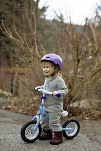 Cute little girl in helmet standing on balance bike on street