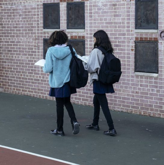 Back view of anonymous children walking and talking about lessons near brick building of school